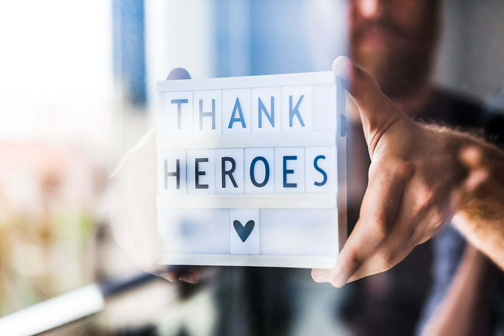 Nurse day concept. Man hands holding lightbox with Thank heroes text thanking doctors, nurses, and medical staff working in hospitals during coronavirus COVID-19 pandemics. View through window glass